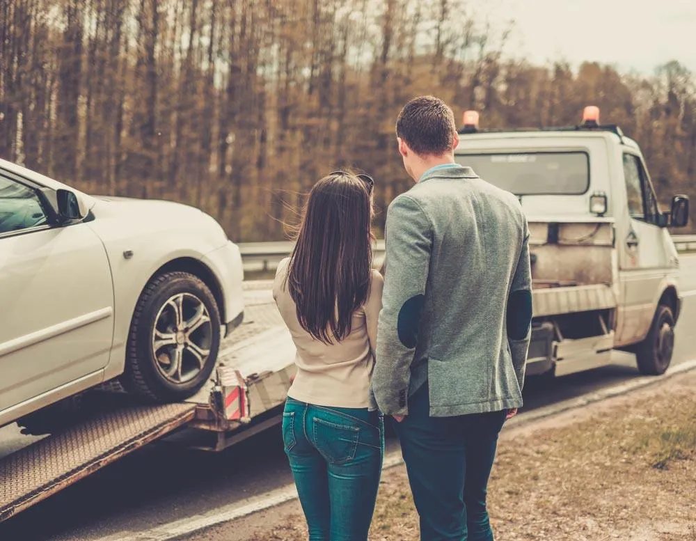 Man and woman looking at their car being towed away after an accident.