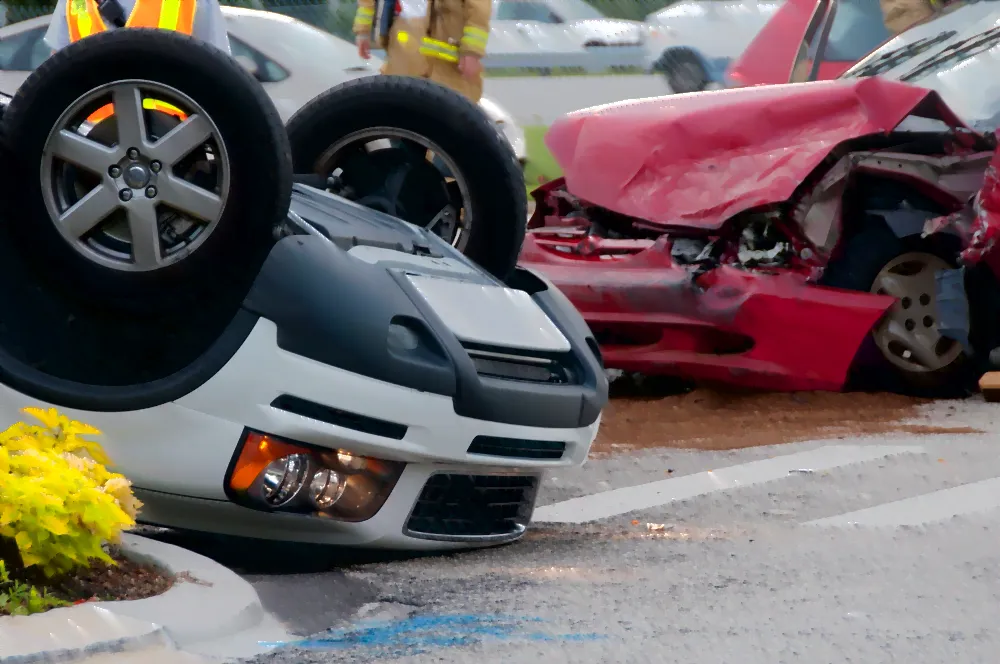 Two cars in an accident one red and crumpled in and one flipped over.