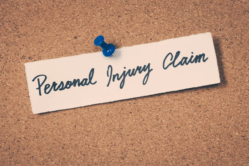 Paper pinned to a board with a thumb tack that says "personal injury claim" in cursive.