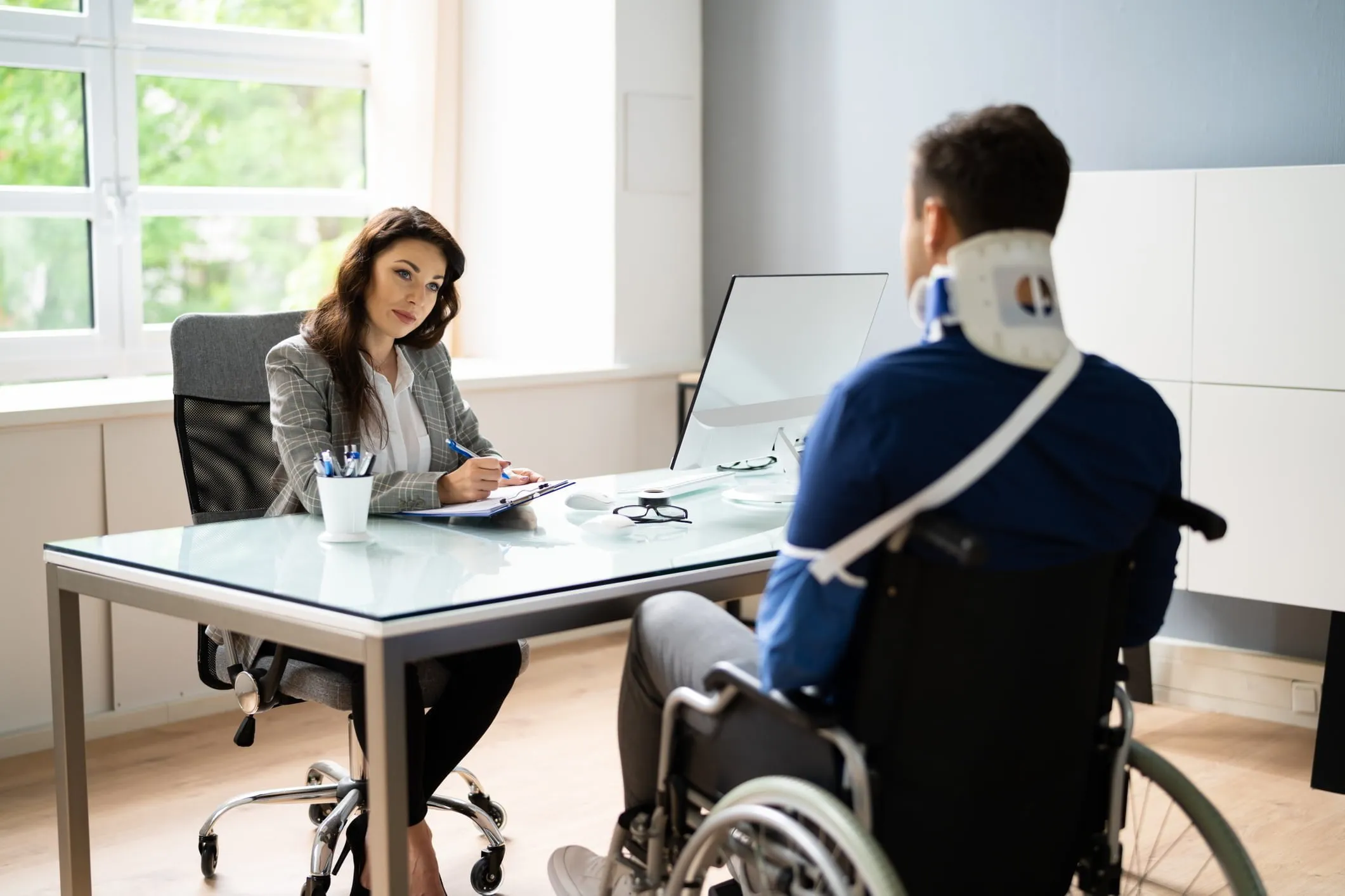 Female lawyer sitting across a desk from a male client in a wheelchair and with a neck brace. Our Wyoming personal injury lawyers fight aggressively for those injured by others. 