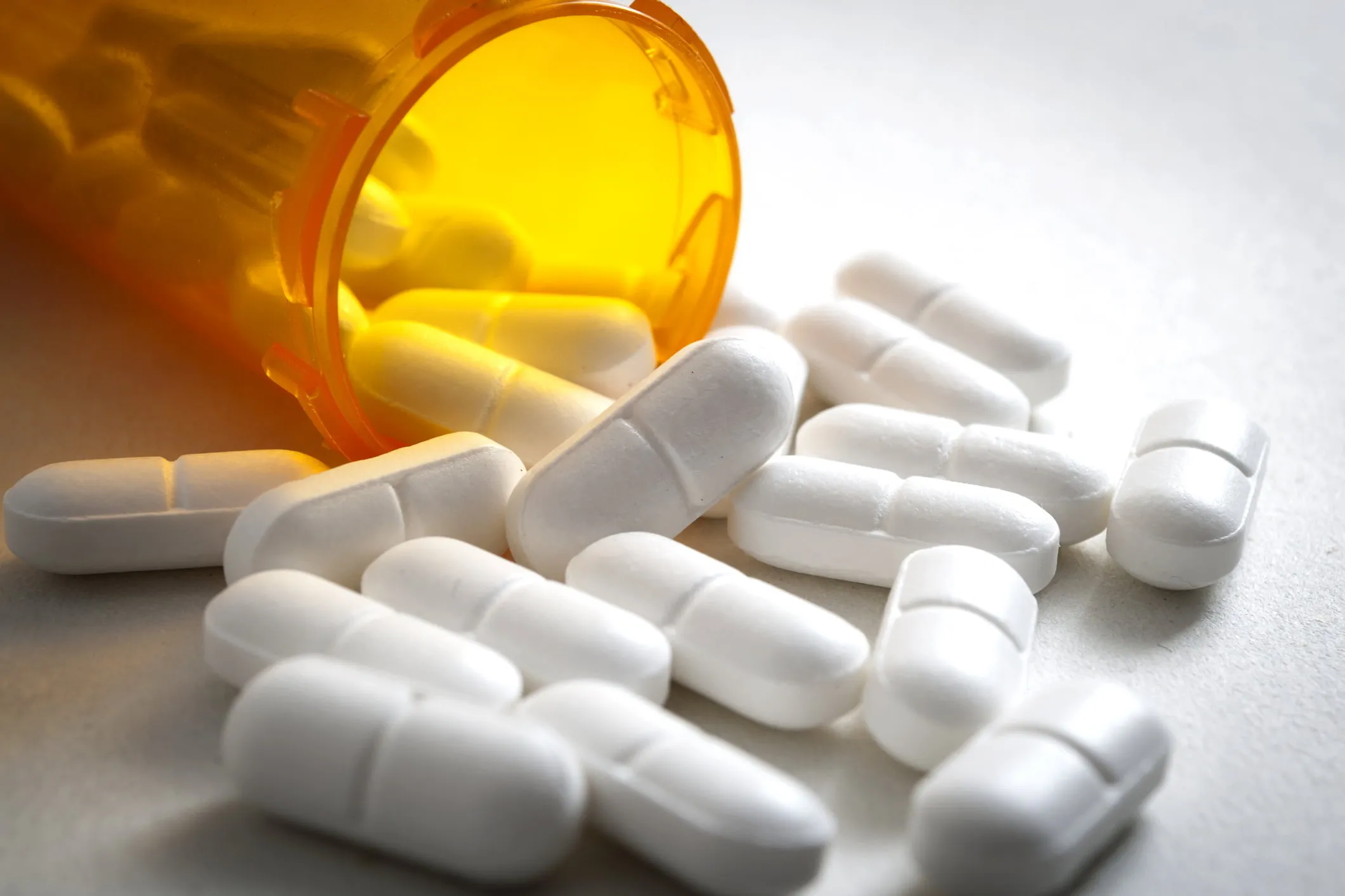White prescription pills falling out of an orange pill bottle. If you have been injured due to a prescription drug, our team of defective drug lawyers is ready to fight for you. 