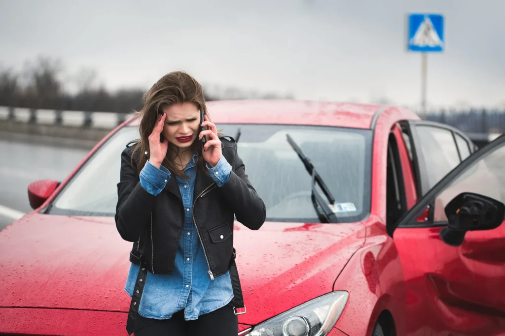 Lady holds head in distress while holding phone to ear as she stands in front of a car wreck. If you have been injured in an accident, contact our personal injury attorney in Cody, WY.