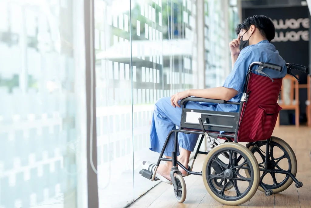 Man touches head as he sits in a wheelchair, sadly looking out a window. If you are suffering from catastrophic injuries, contact our Wyoming personal injury lawyer.