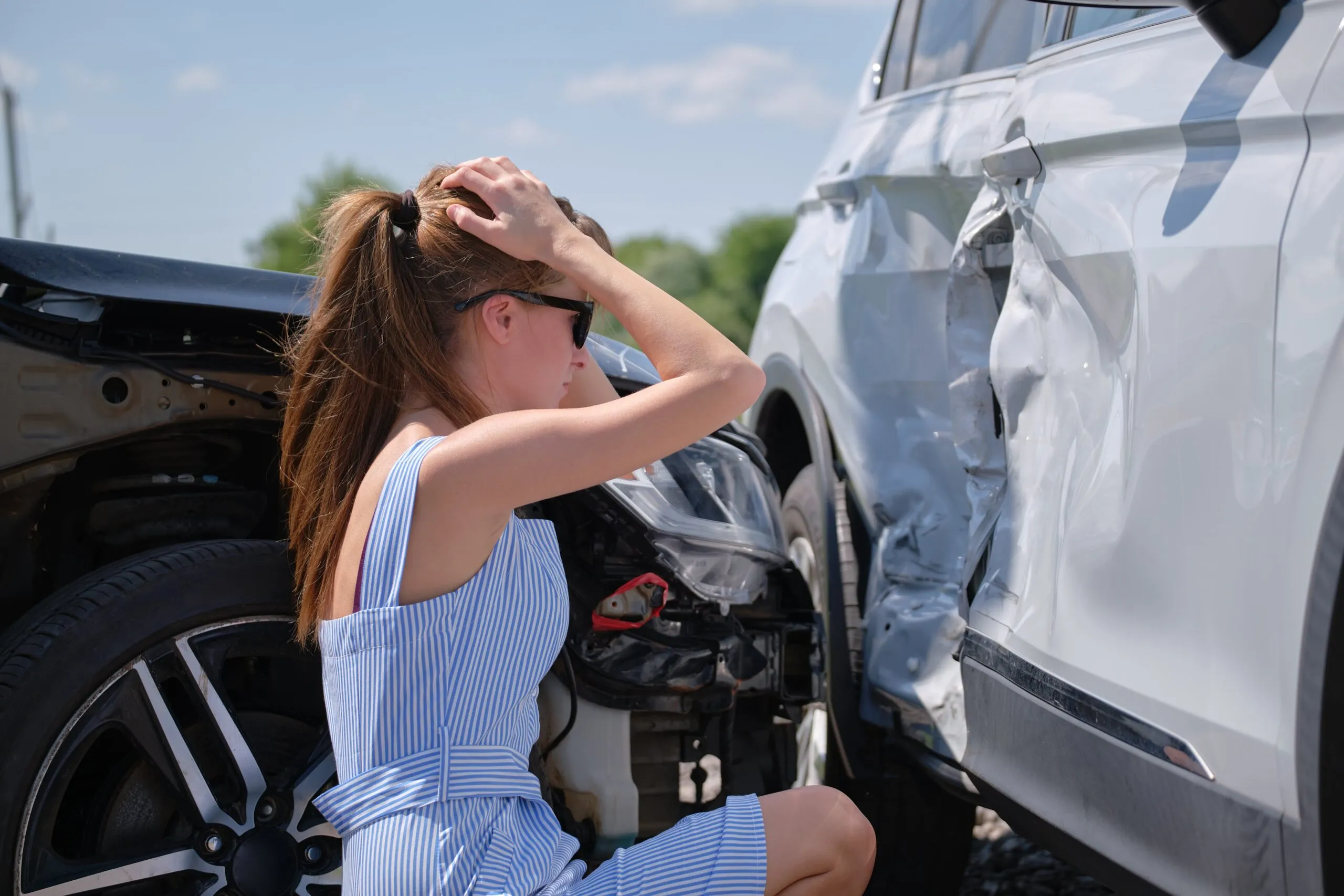 Distressed woman driver sitting on street side, staring at her damaged car. Contact our vehicle accident lawyer if you’ve been injured in a motor vehicle accident.