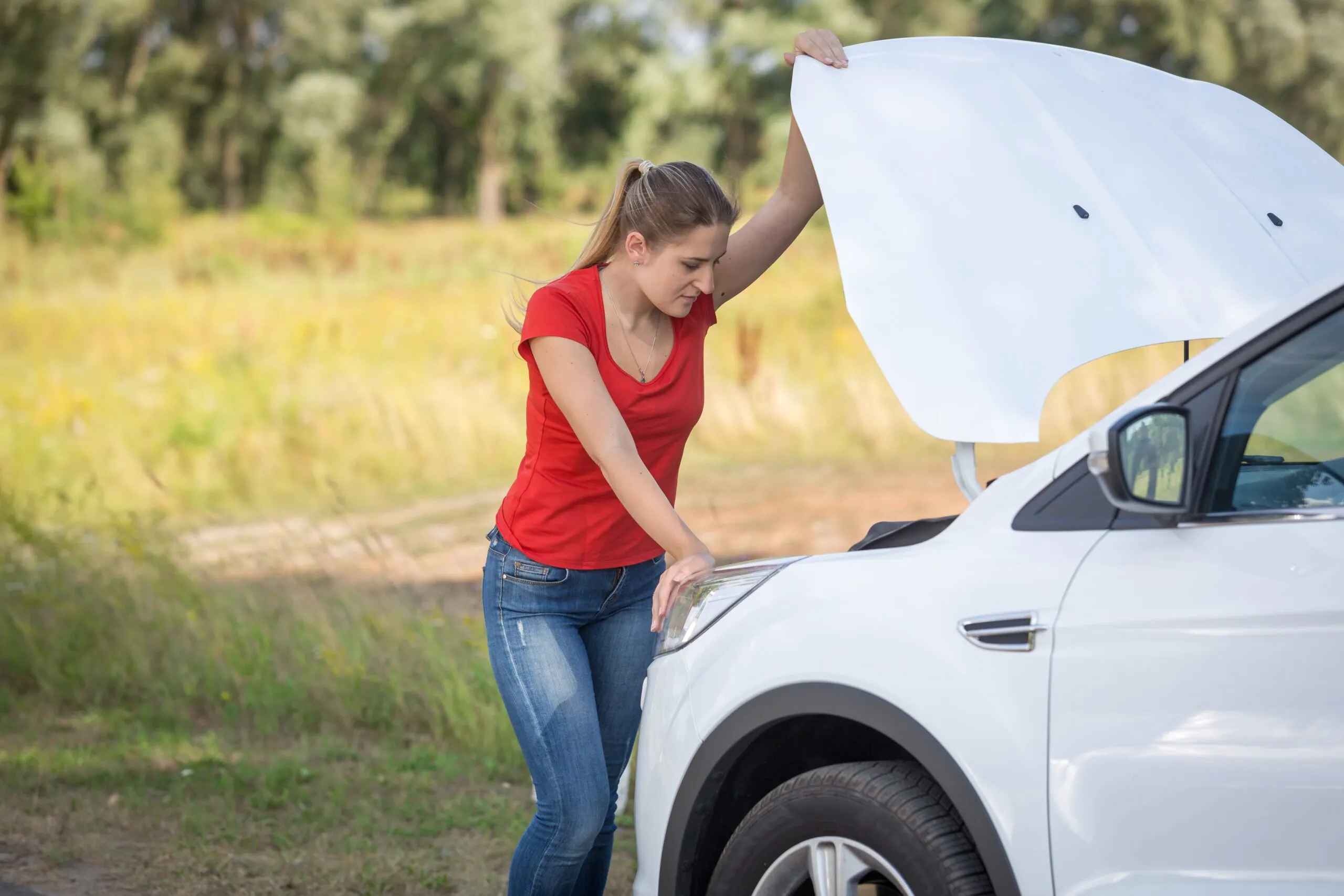 Woman looks at broken car’s engine in field. If your motor vehicle is defective, contact us for the auto product liability defect lawyers in Wyoming that will fight to get you proper compensation.